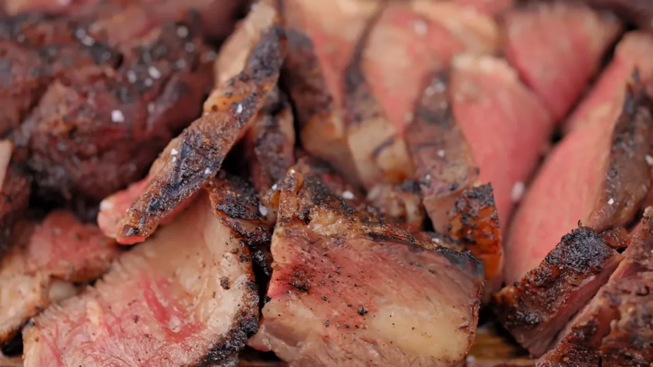 Sliced tomahawk steak with pink centers and dark browned edges piled on a wooden board