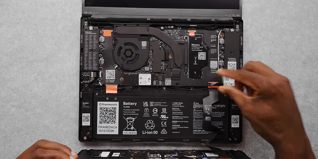 An open Framework laptop with exposed internal components and a detached input cover below it