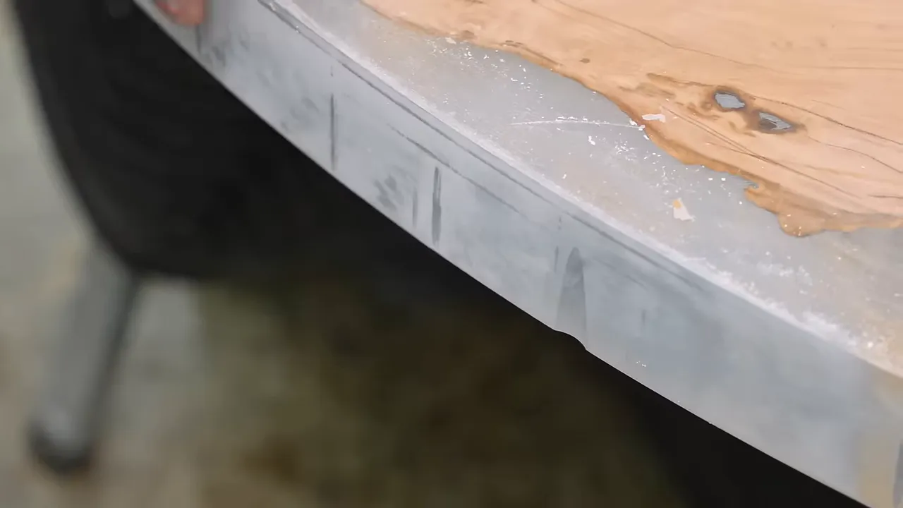 Hands indicating a gouge in the translucent epoxy edge of the round tabletop