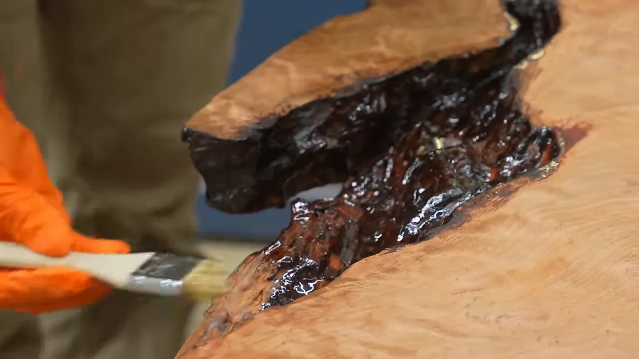 Orange-gloved hands brushing epoxy into an irregular redwood live edge