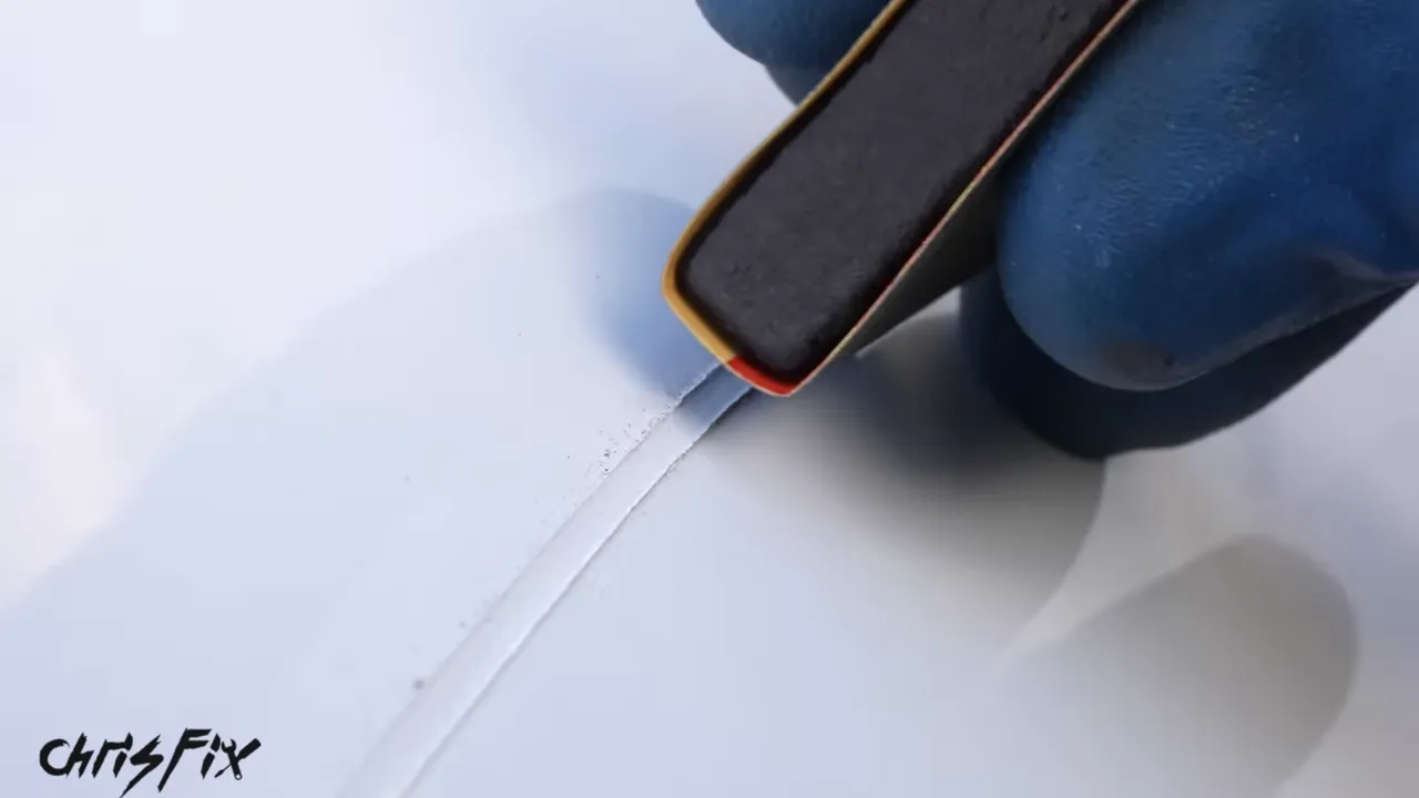 Small sanding block wrapped in sandpaper positioned along the raised touch-up paint