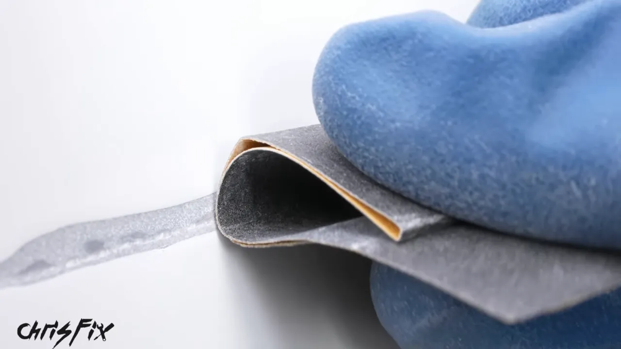 Rounded loop of sandpaper held against a scratch in white paint