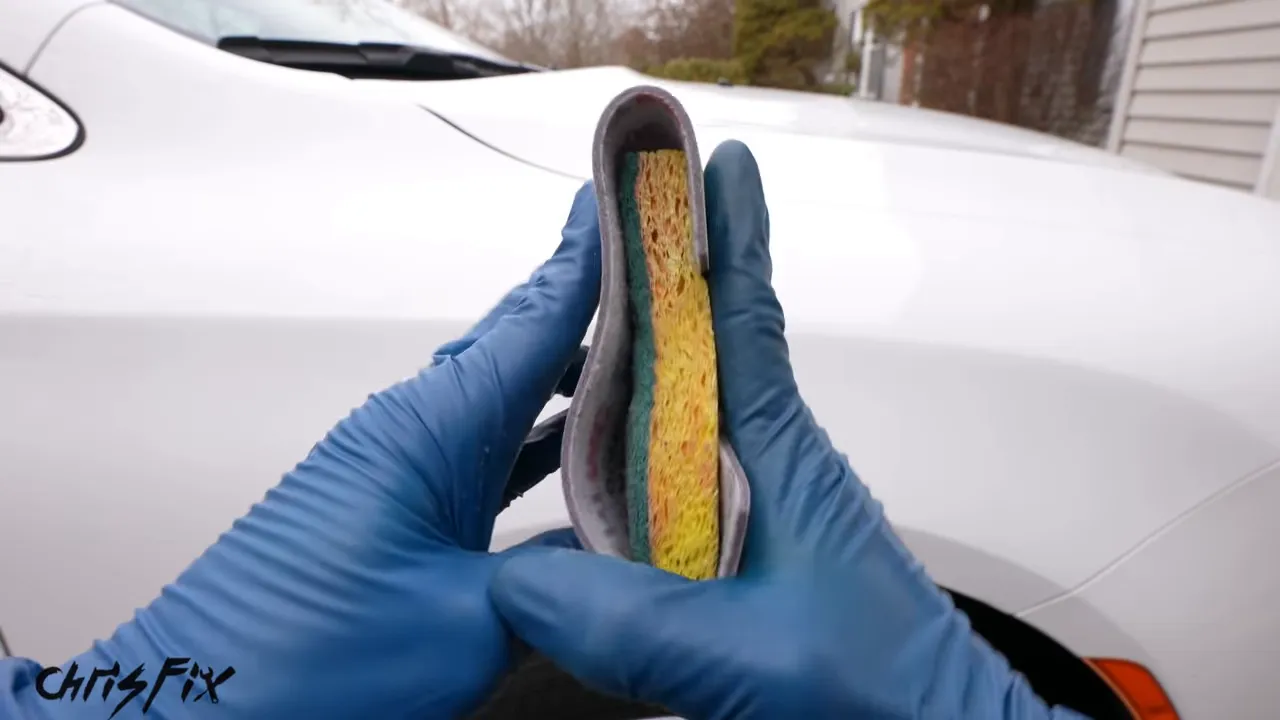 Sandpaper wrapped around a yellow sponge held in blue-gloved hands