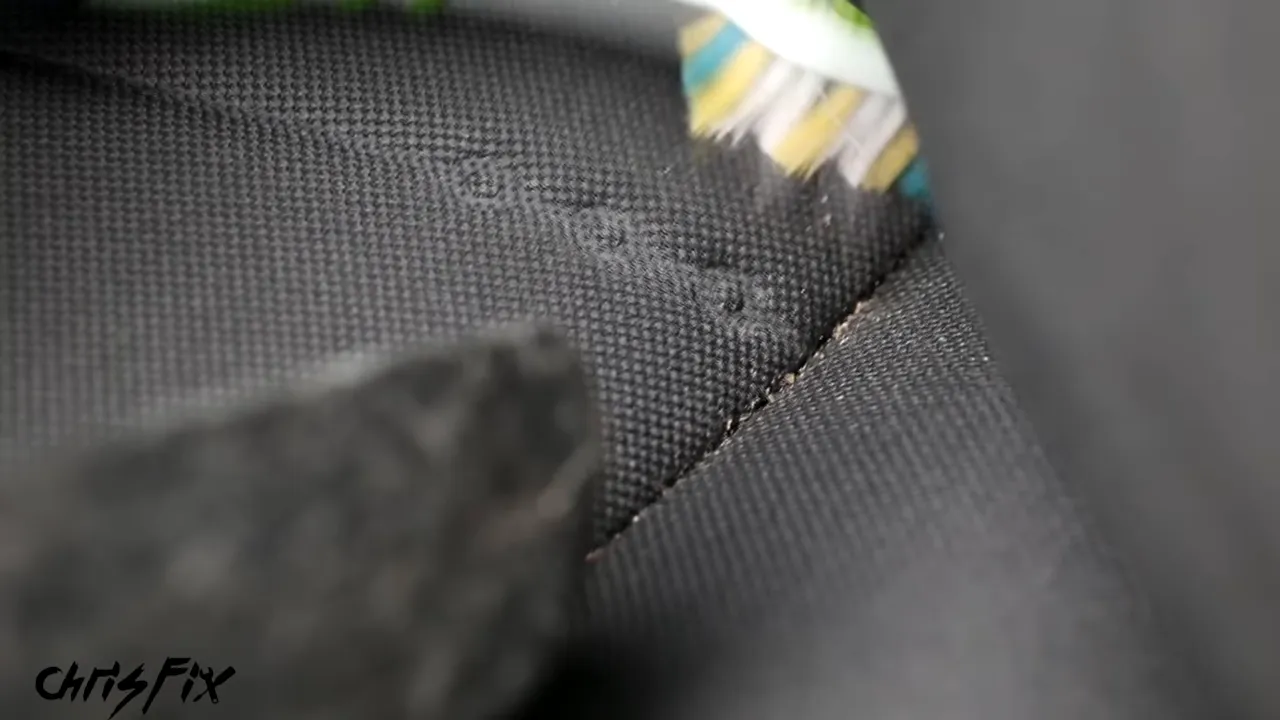 Toothbrush loosening dirt from a cloth seat seam beside a vacuum nozzle