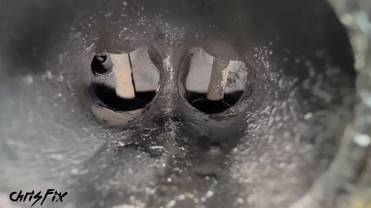 Close-up inside an exhaust port showing two valve stems and wet dark deposits around the right valve