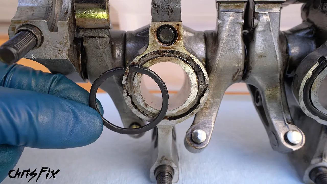 Gloved hands holding old flattened seals beside the underside of the rocker arm assembly