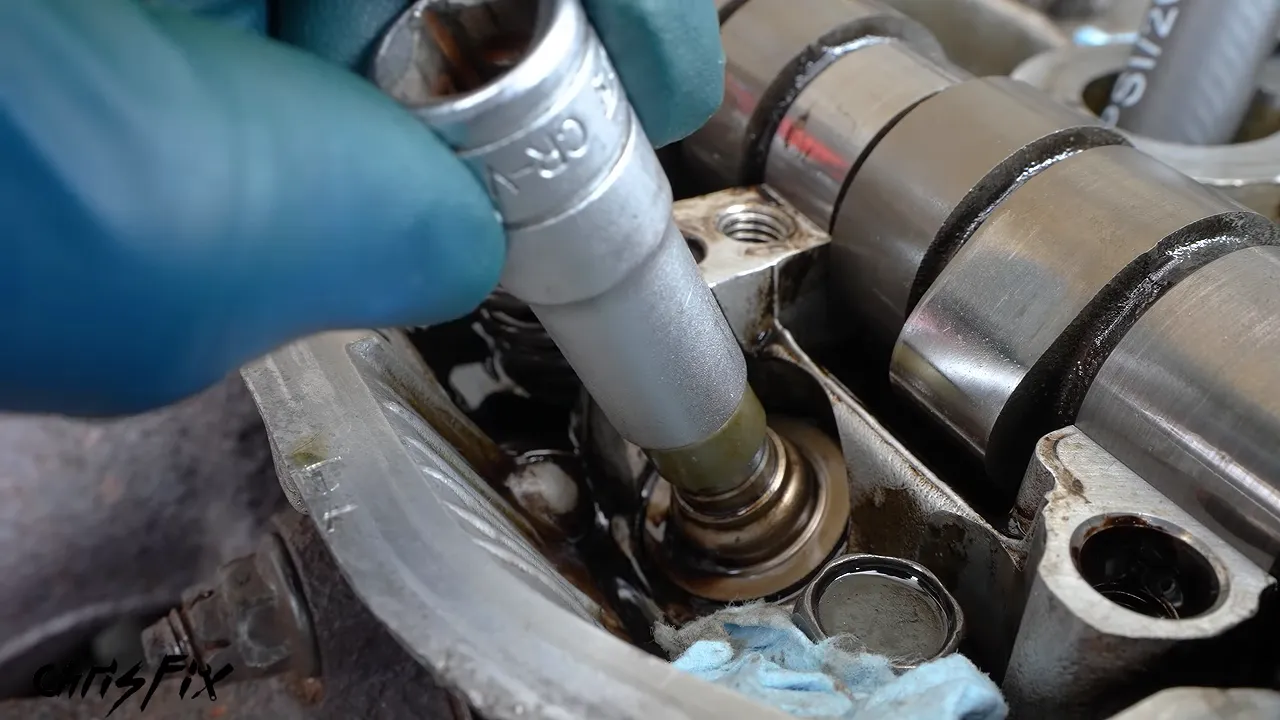 Deep socket positioned over a green valve stem seal with a gloved finger pointing toward its base