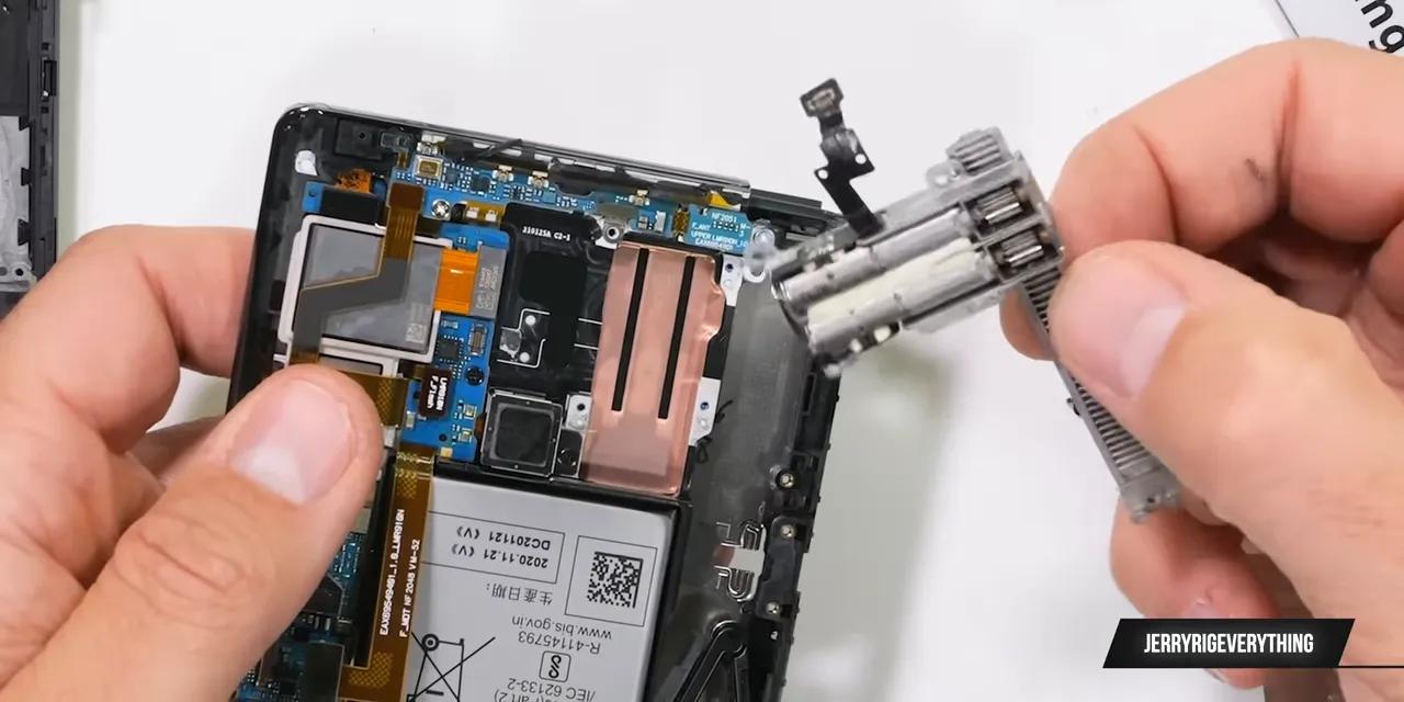 Disassembled LG rollable phone with a removed motor assembly held beside its exposed internals