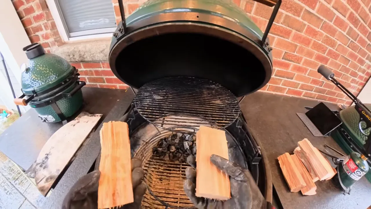 Open Big Green Egg with small wood splits arranged at the front of the charcoal basket