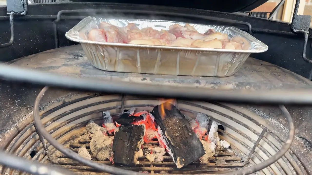 Small flames and glowing coals beneath the raised grill rack and a pan of brisket trimmings