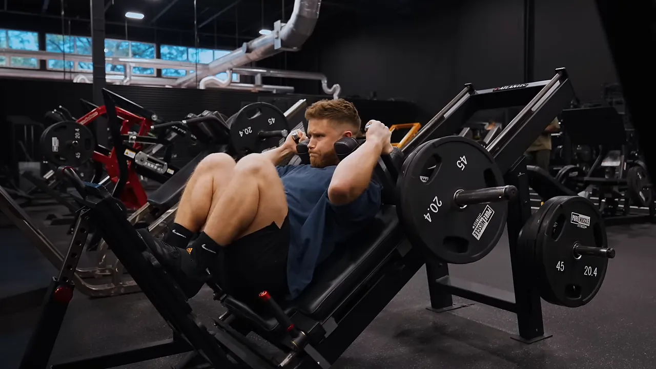 Lifter at the bottom of a hack squat with deeply bent knees and back supported by the machine