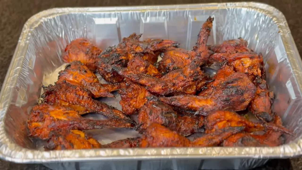 Foil tray filled with browned chicken wings coated in orange-red sauce