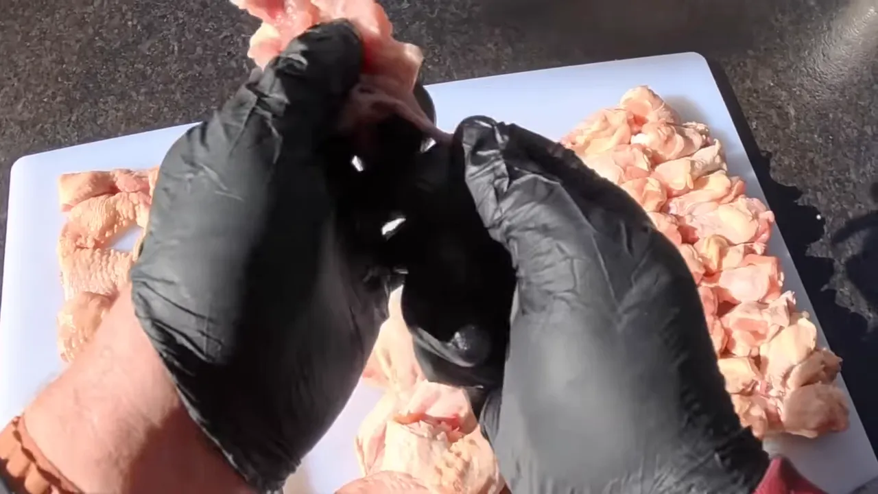 Gloved hands pulling an exposed bone from a chicken wing over a cutting board