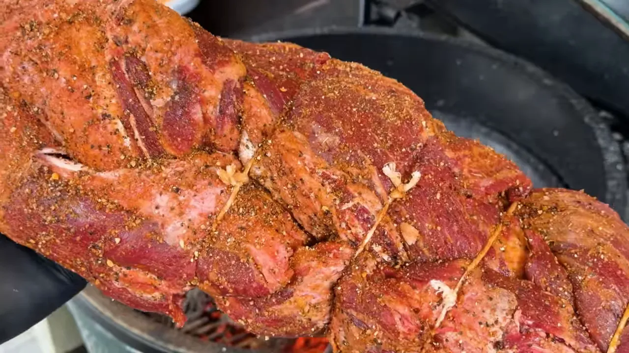 Seasoned braided beef tenderloin secured with butcher’s twine above a charcoal bed