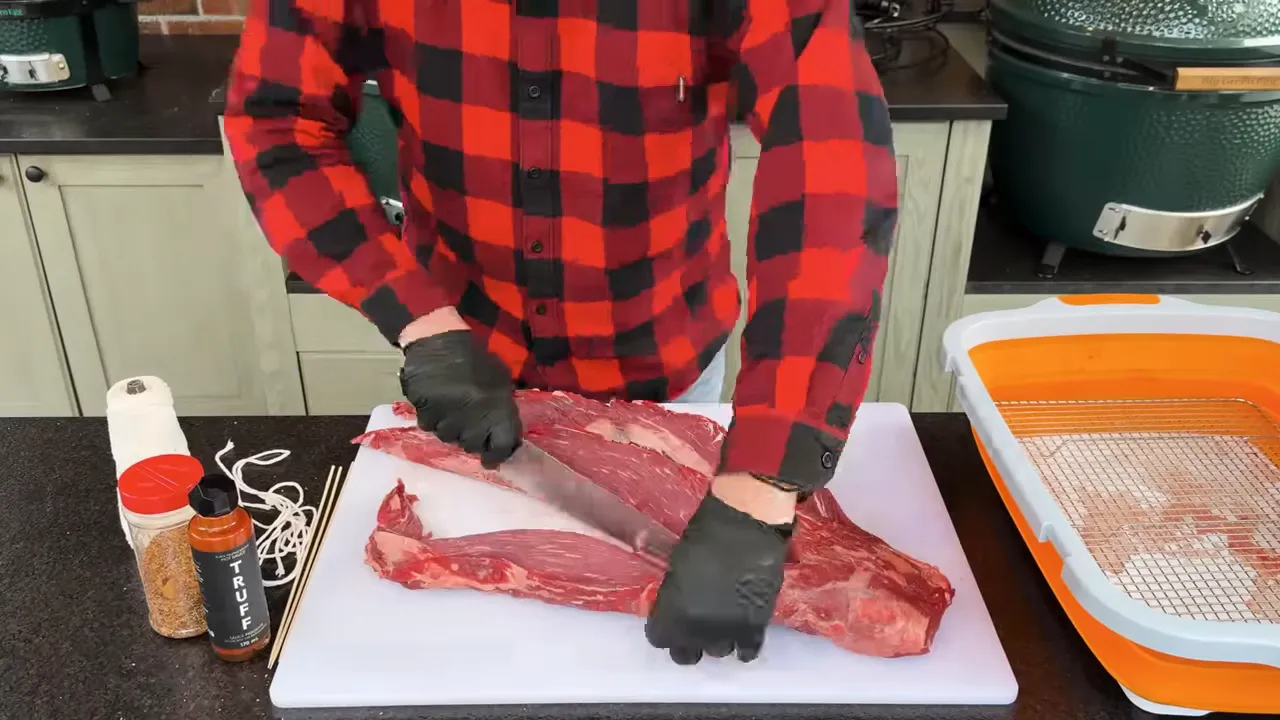 Beef tenderloin divided lengthwise into three strands on a white cutting board