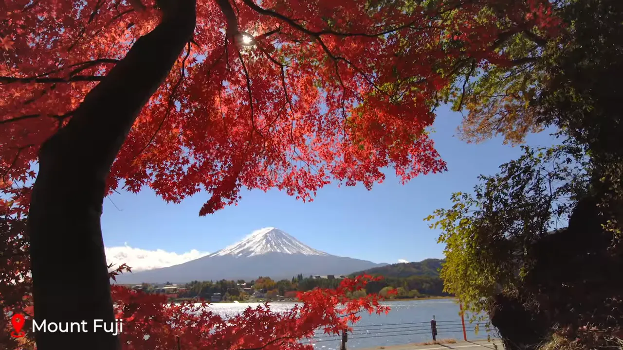 Mount Fuji framed by red autumn maple leaves over Lake Kawaguchi, snow-capped peak under a clear blue sky
