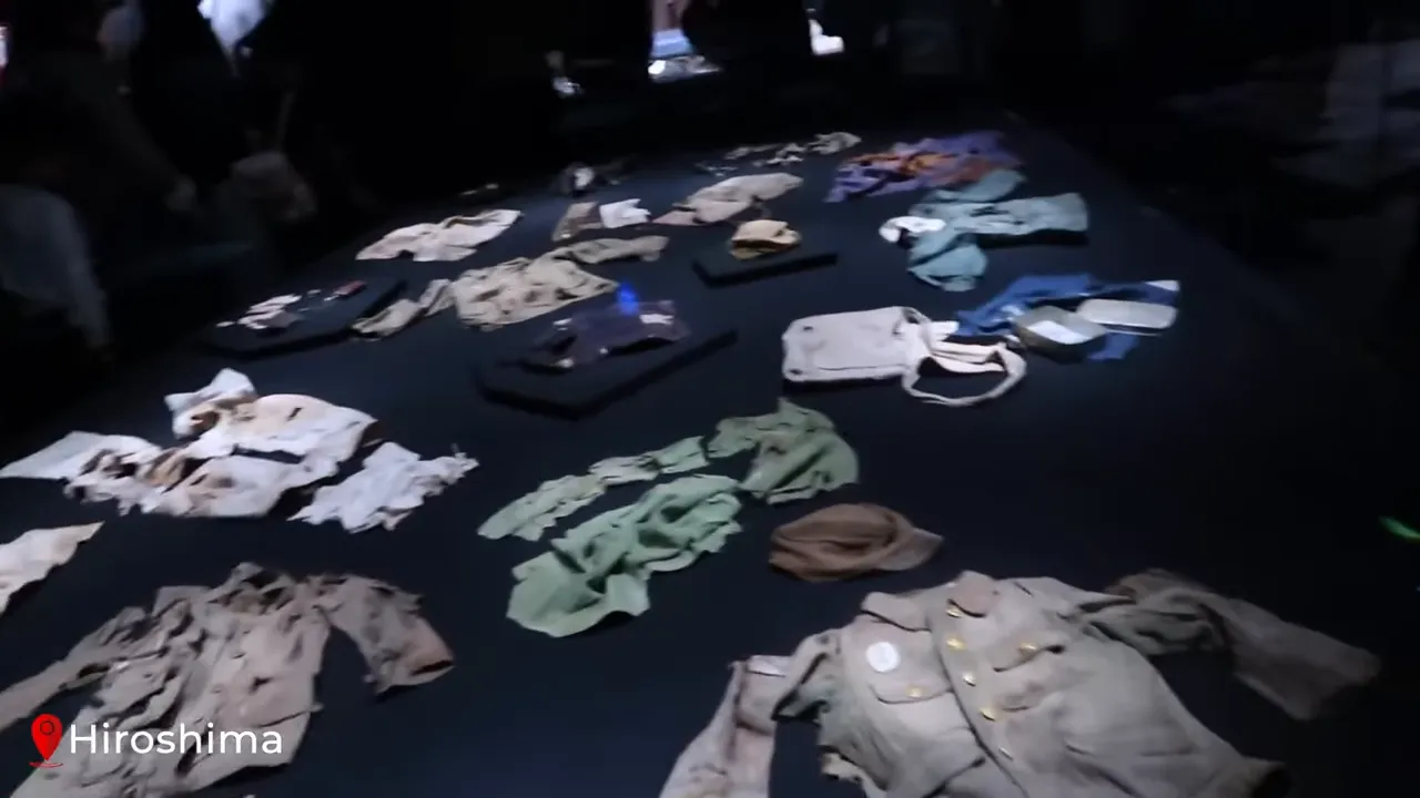 Damaged clothing and uniforms arranged in a dimly lit exhibit at the Hiroshima Peace Memorial Museum