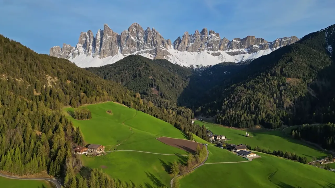 Panoramic view of Dolomite spires towering over lush green meadows and wooded valleys