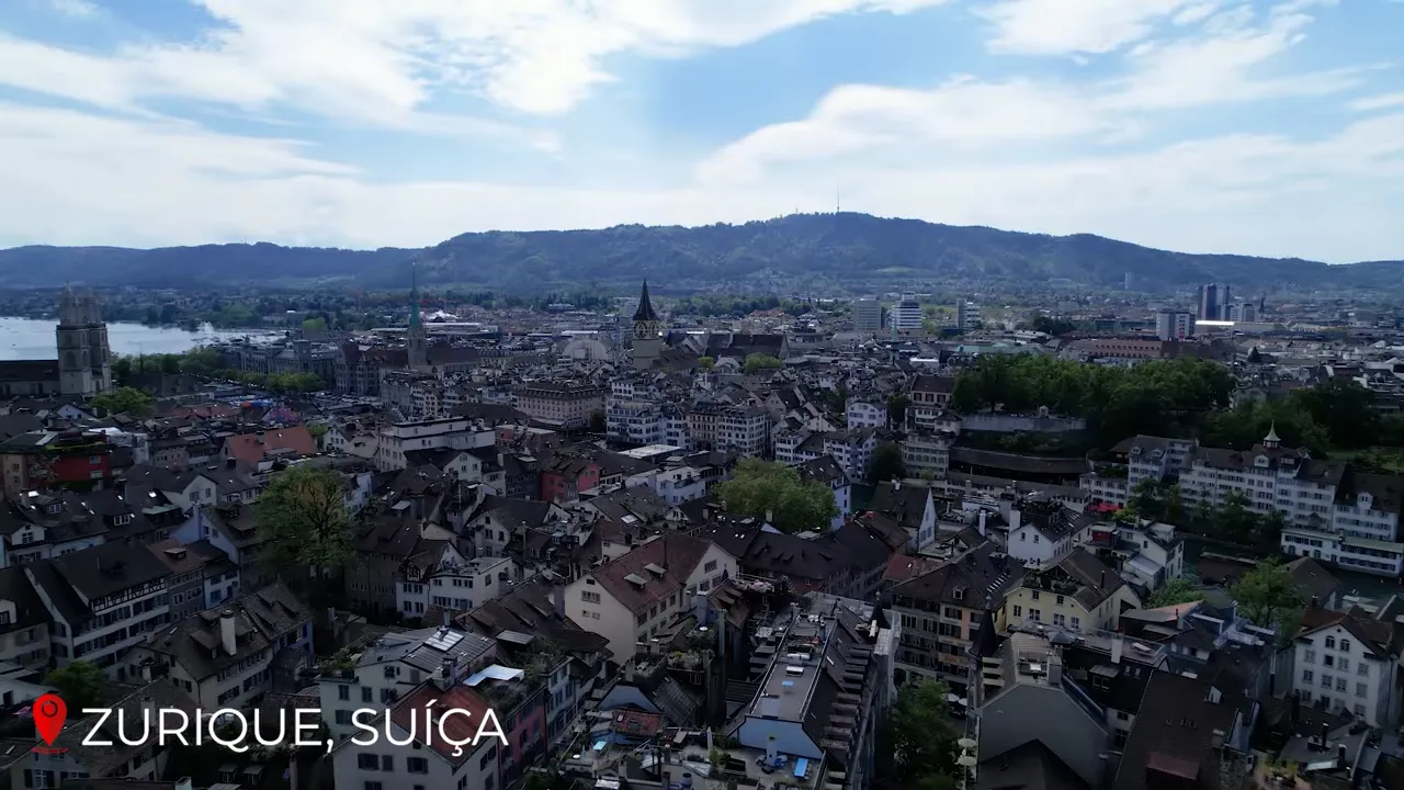 Panoramic aerial view of Zurich showing city rooftops, Lake Zurich and distant hills under a blue sky