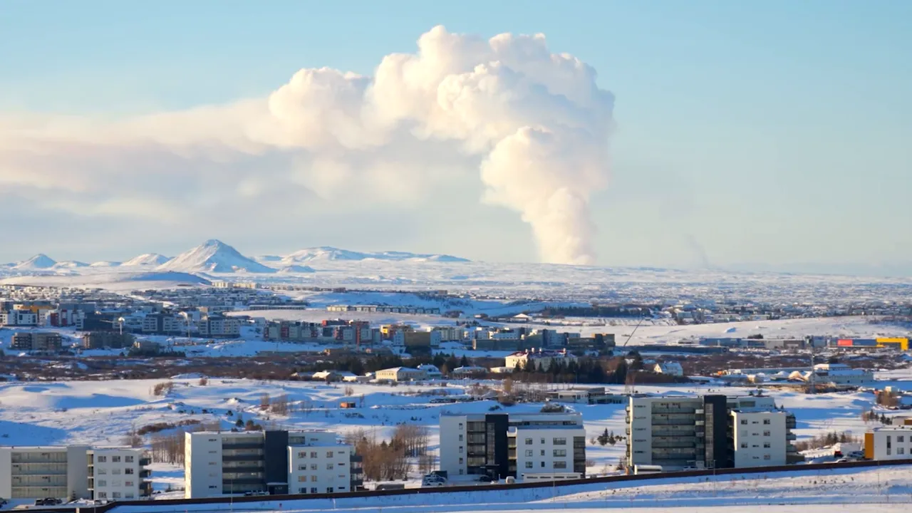 Panoramic winter skyline with snow-covered neighbourhoods, low mountains and a large geothermal steam plume rising against a pale blue sky