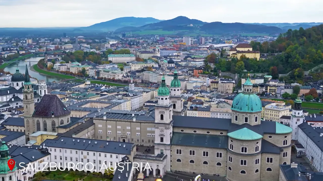 Wide aerial panorama of Salzburg showing green cathedral domes, baroque rooftops and the Salzach river