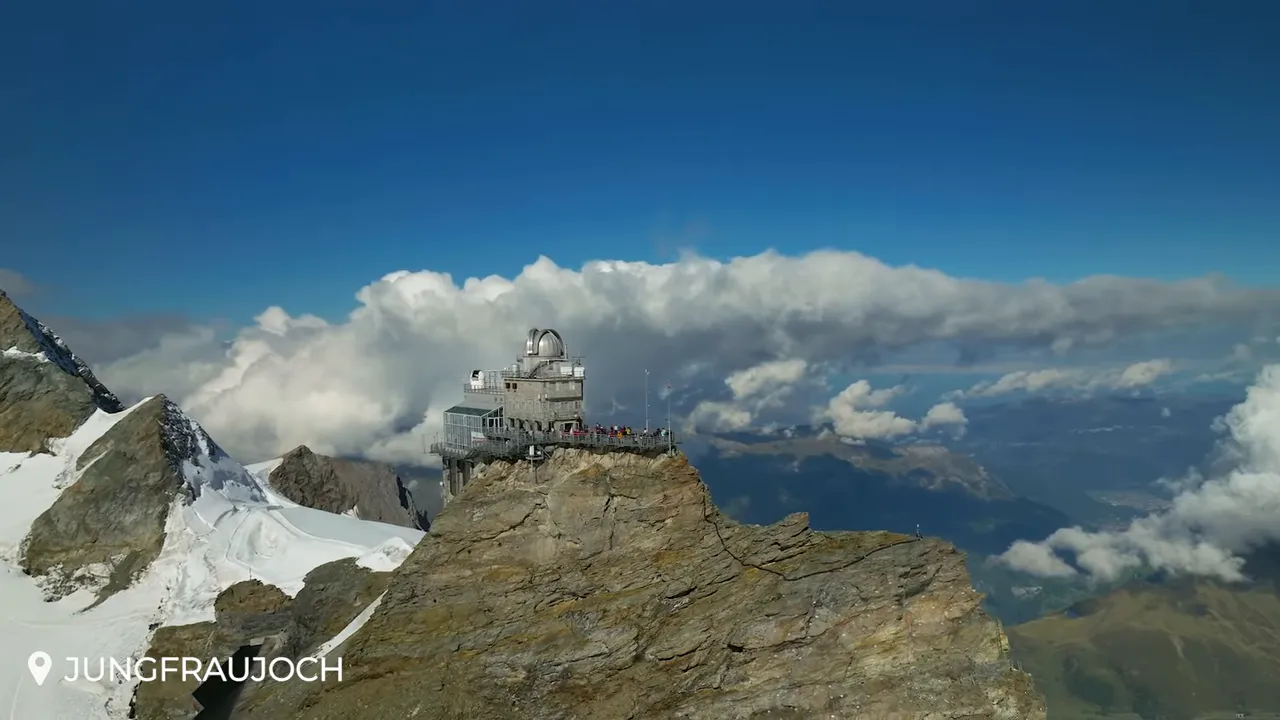 Clear high-resolution view of the Jungfraujoch Sphinx observatory on a rocky promontory with glacier, distant valley and expansive clouds