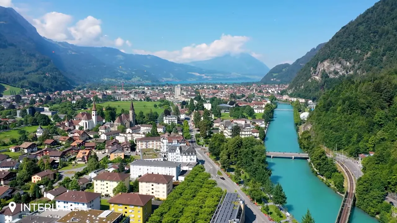 Aerial view of Interlaken town with a turquoise river, bridges, lakes and surrounding mountains under a clear sky.