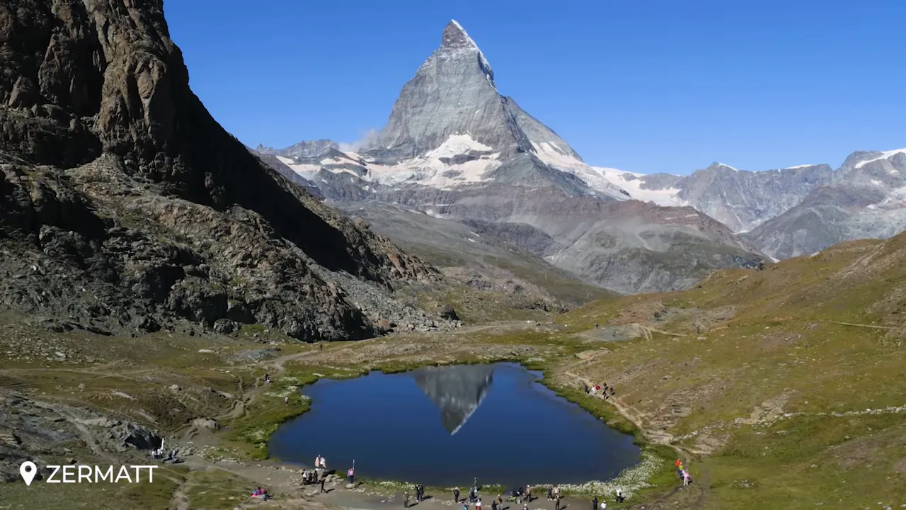 Matterhorn peak and its reflection in Riffelsee near Zermatt with alpine foreground and clear blue sky