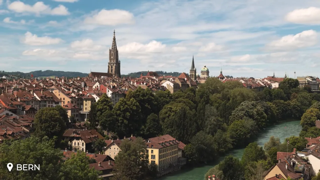 Clear aerial panorama of Bern’s Old Town with the cathedral spire and the Aare River running beside historic red-roofed buildings.