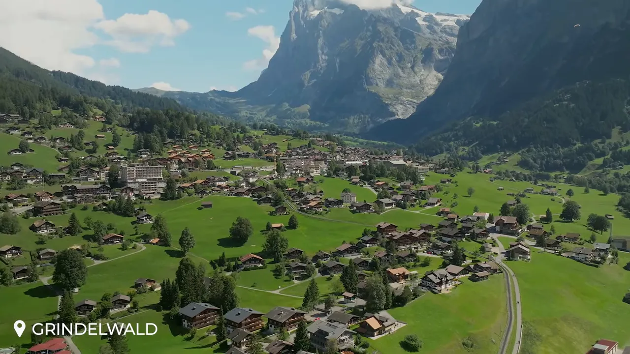 Aerial view of Grindelwald village with chalets, rolling green fields and a steep mountain backdrop
