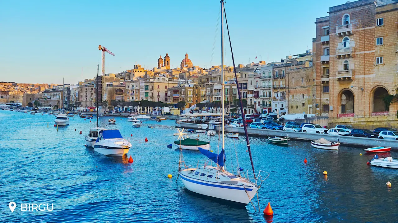 Birgu harbour with moored sailboats, blue water and historic limestone buildings on the waterfront