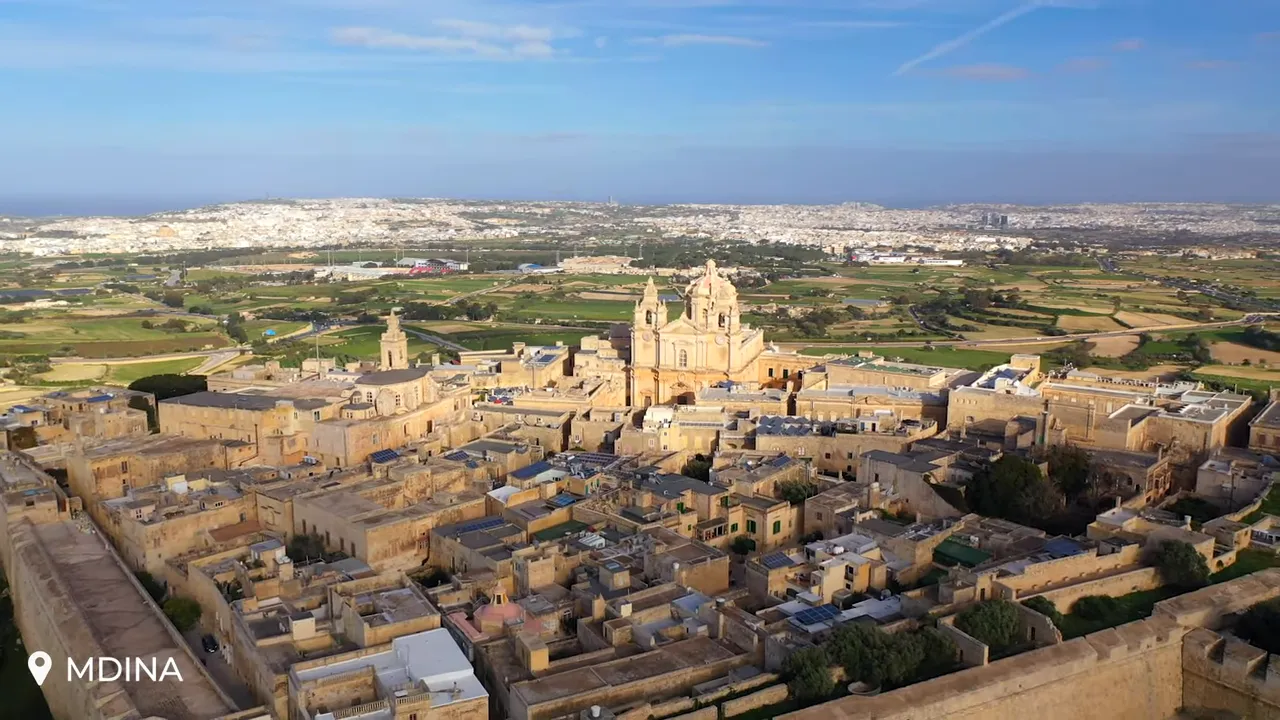 High-resolution aerial shot of Mdina showing the city walls, cathedral and dense historic rooftops with countryside beyond