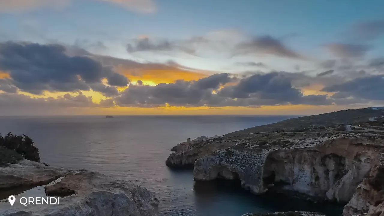 Wide sunset view of Qrendi coastline with limestone cliffs, sea caves and a dramatic sky