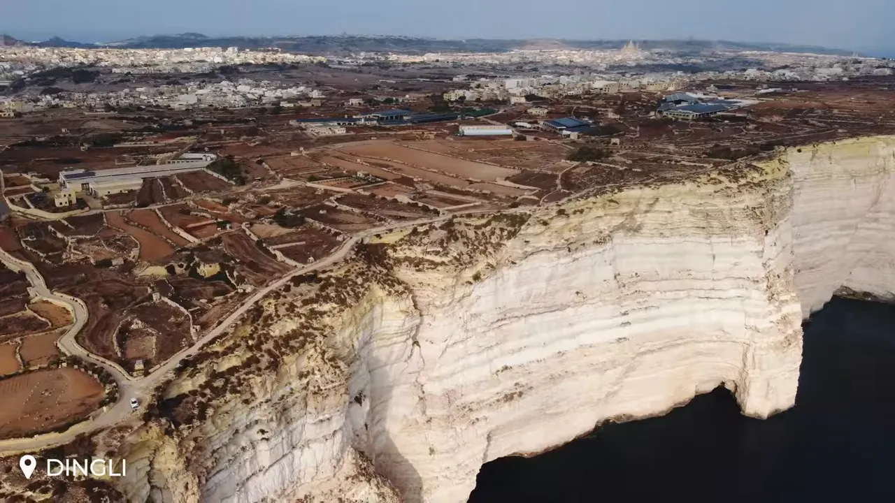 Wide aerial panorama of Dingli Cliffs with steep white limestone faces and patchwork terraced fields inland