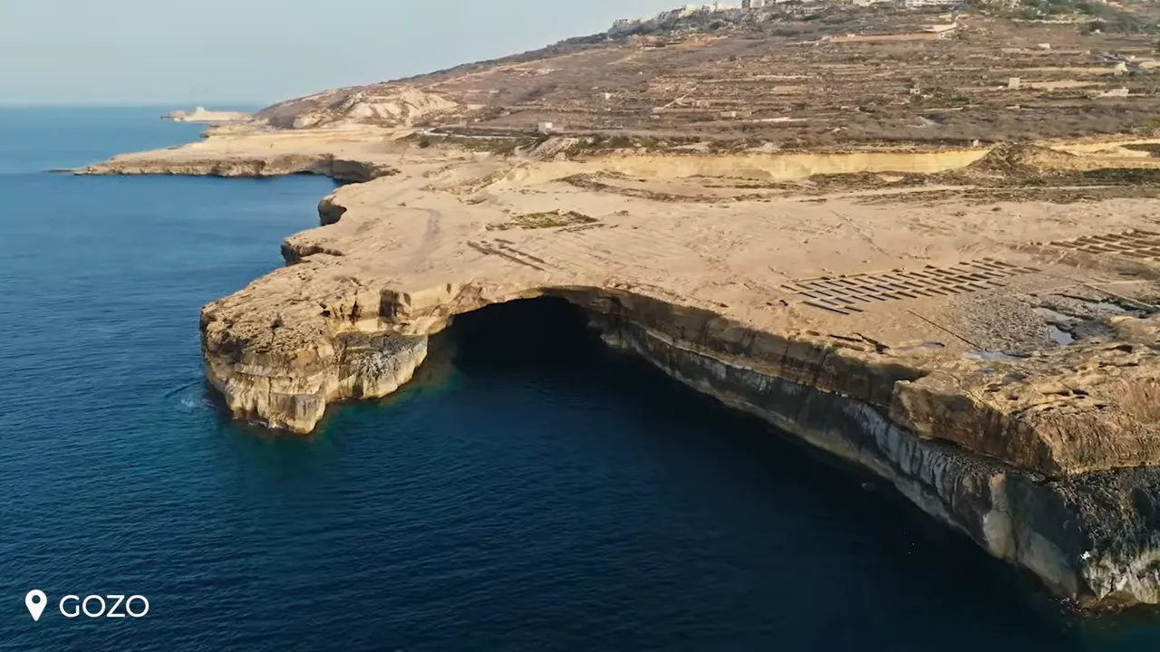 Aerial view of Gozo coastline with limestone cliffs and a large sea cave opening into deep blue Mediterranean water