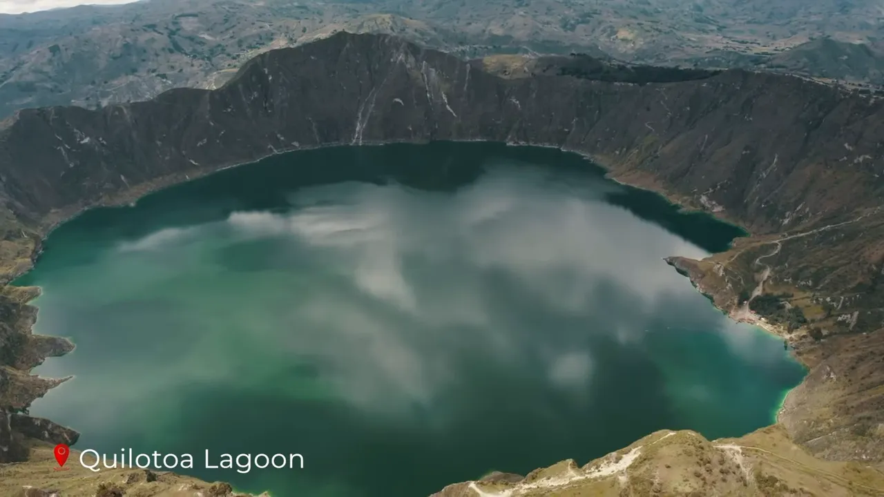 Panoramic aerial shot of Quilotoa lagoon with vivid turquoise water, cloud reflections and the Andean crater rim