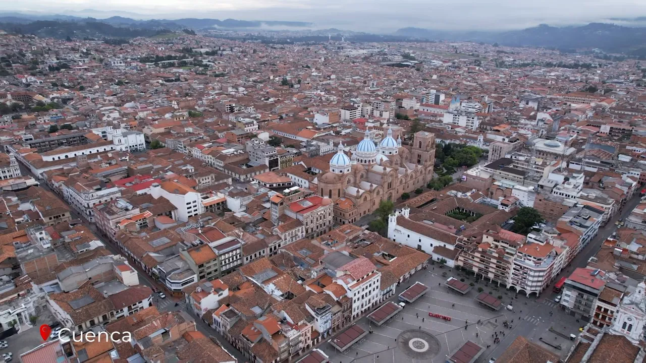 Wide aerial panorama of Cuenca showing the cathedral’s blue domes, central plaza and sprawling colonial rooftops
