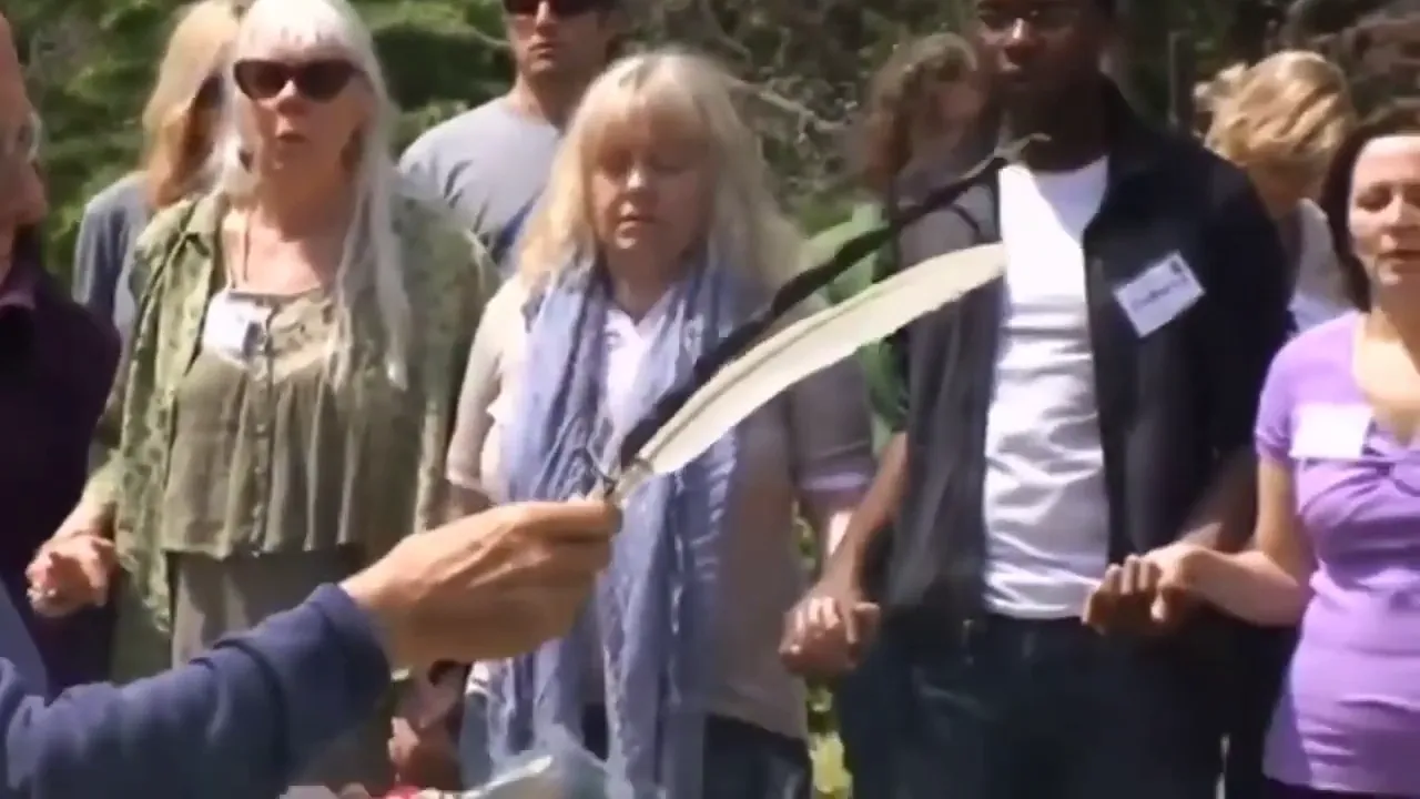 Mano sosteniendo una pluma grande frente a un grupo de personas tomadas de la mano en un taller al aire libre