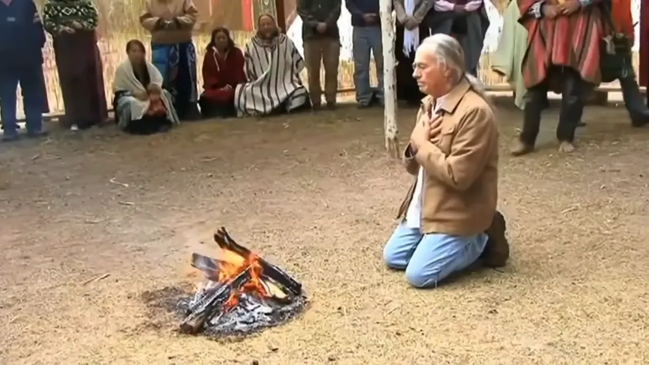 vista amplia de una ceremonia con el maestro arrodillado frente a la hoguera y personas alrededor