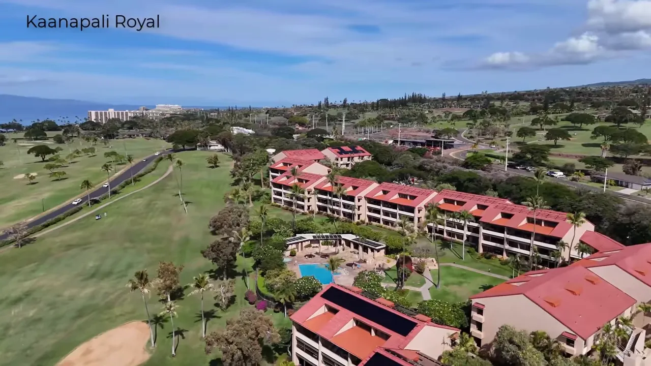 Aerial view of Kopali Royal condominium buildings fronting the Kapalua golf course showing the central pool, red roofs and shoreline hotels in the distance.