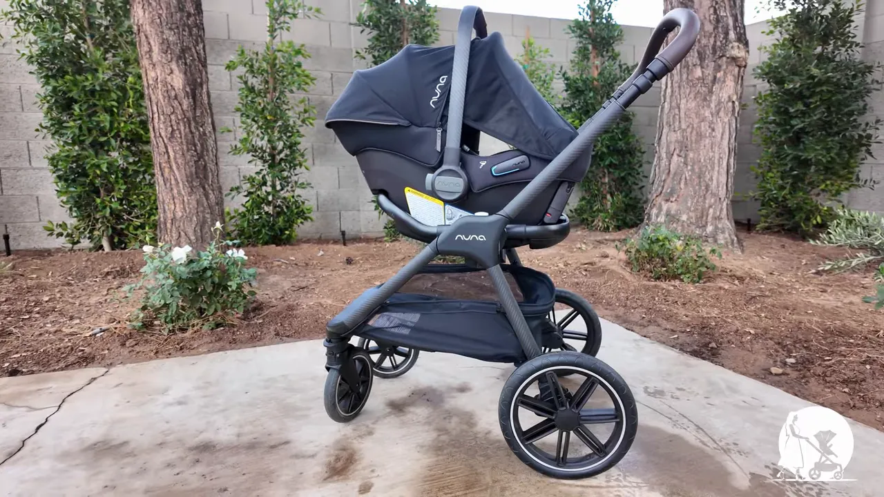 Side profile of Nuna TRIV LX stroller with PIPA URBN car seat attached, showing large rear wheel, underbasket and carbon-fiber reinforced frame.