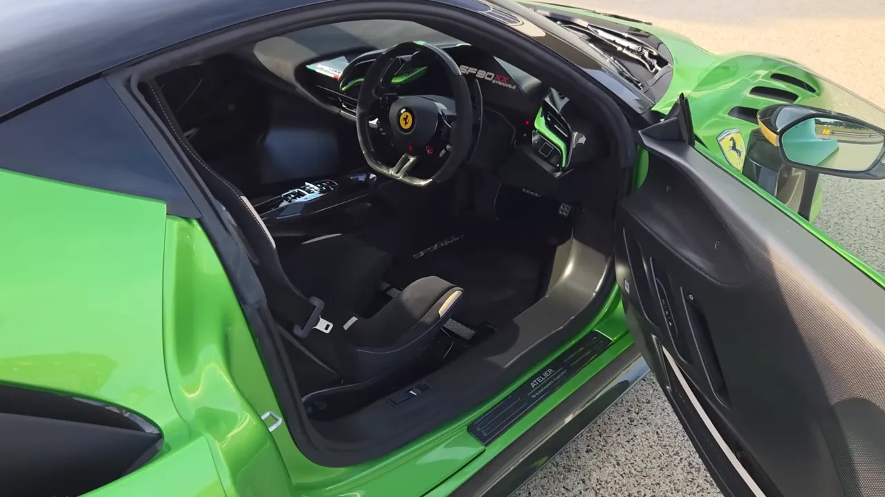 Vista interna della Ferrari SF90 XX con porta aperta, sedile in carbonio, volante e placca Atelier sulla soglia