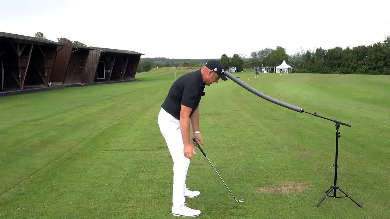 Instructor at address with foam noodle touching head demonstrating head-out posture and shoulder tilt