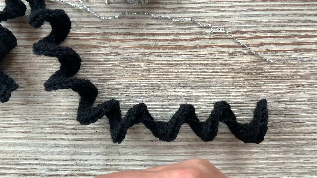Long black crochet strip curled into repeated waves on a pale work surface