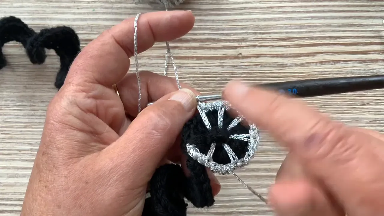 Hands holding a black crochet curl with silver stitches radiating from its inner edge