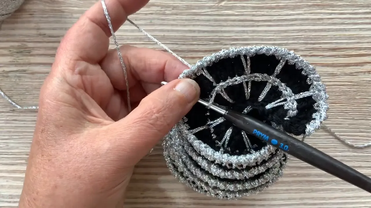 Hands holding a stacked black and silver crochet spiral with a silver line along the inner web edge