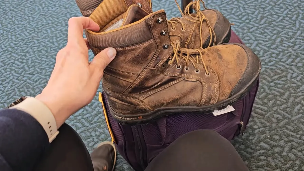 Off grid life - large work boots sitting on top of a purple rolling bag at the airport