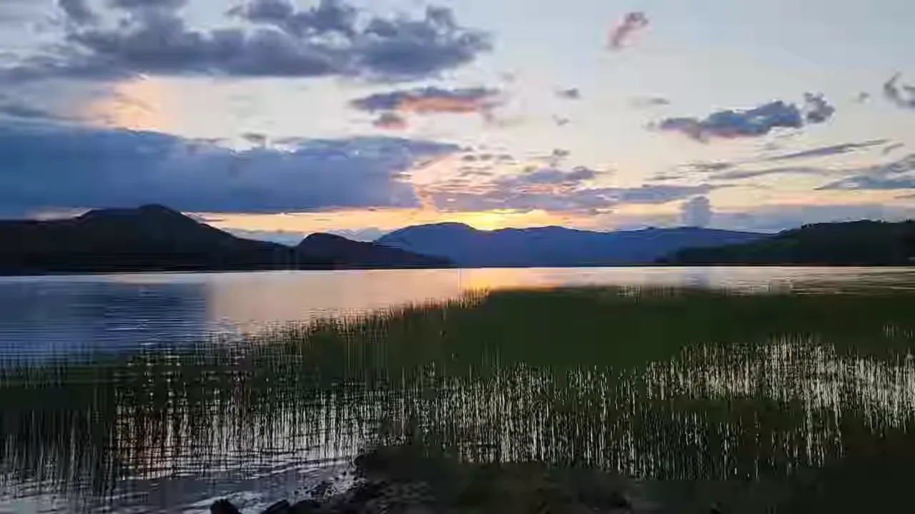 Off grid life - sunset over calm lake water with reeds in the foreground and mountains beyond