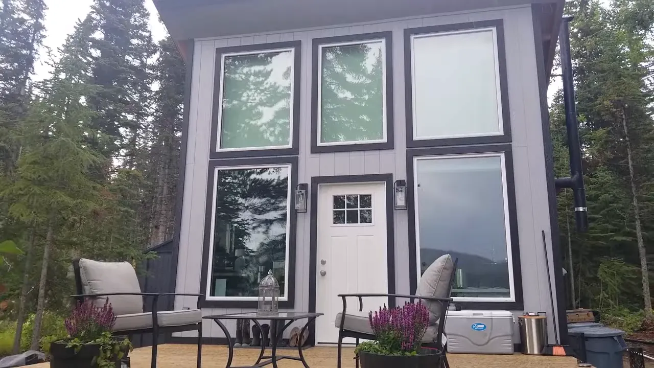 Off grid life - full front view of the tiny cabin with dark trim, tall windows, and finished deck