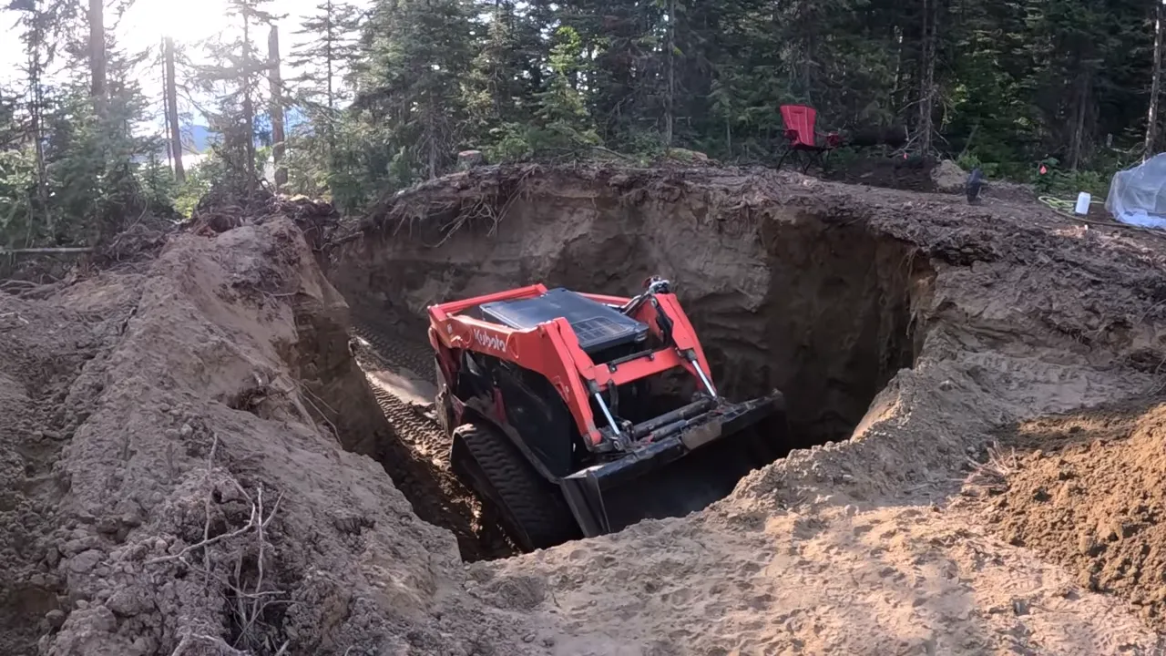 Off grid life - compact track loader working at the edge of a deep pit with sandy walls